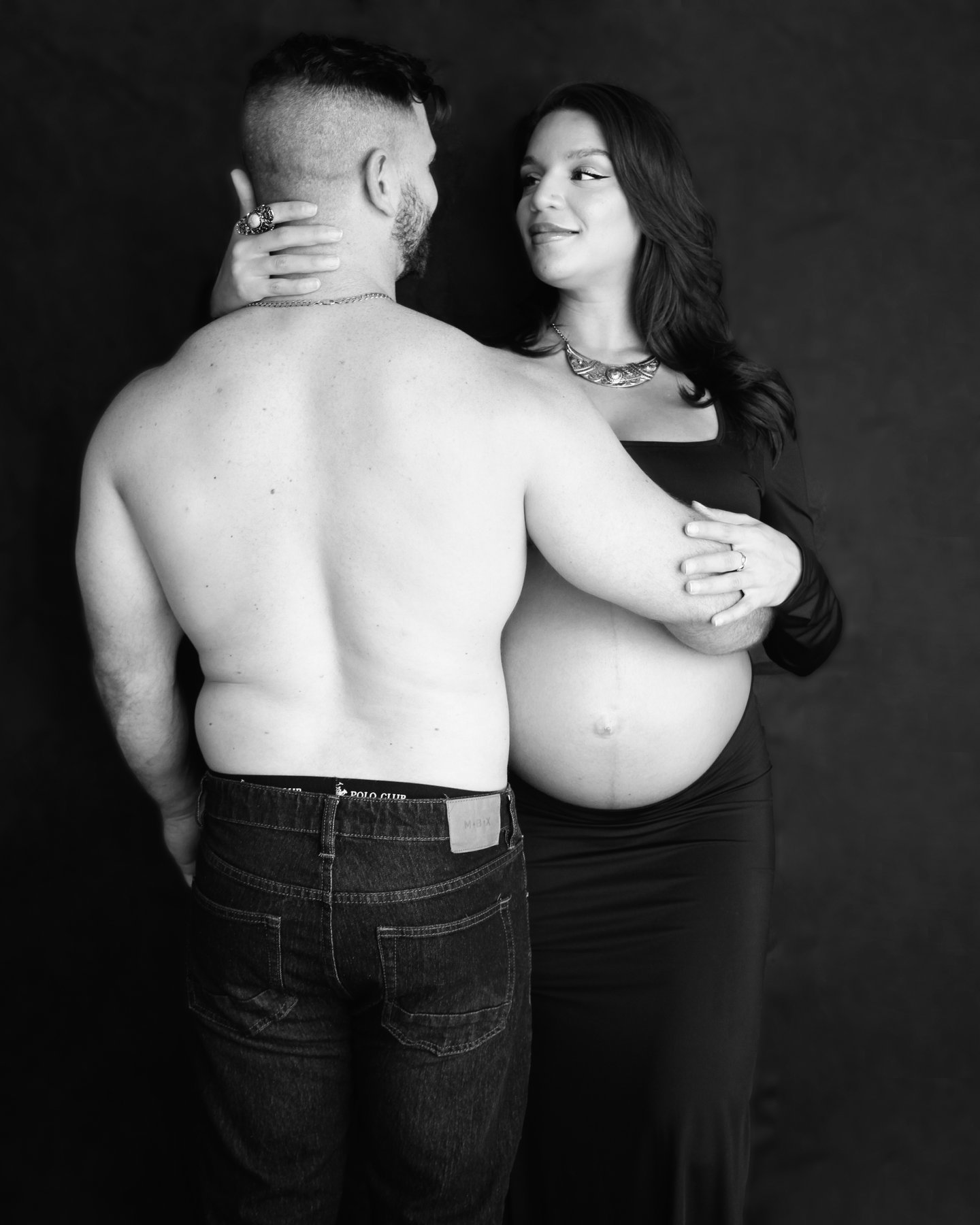 Black-and-white photograph of an expectant couple, the father's back to the camera