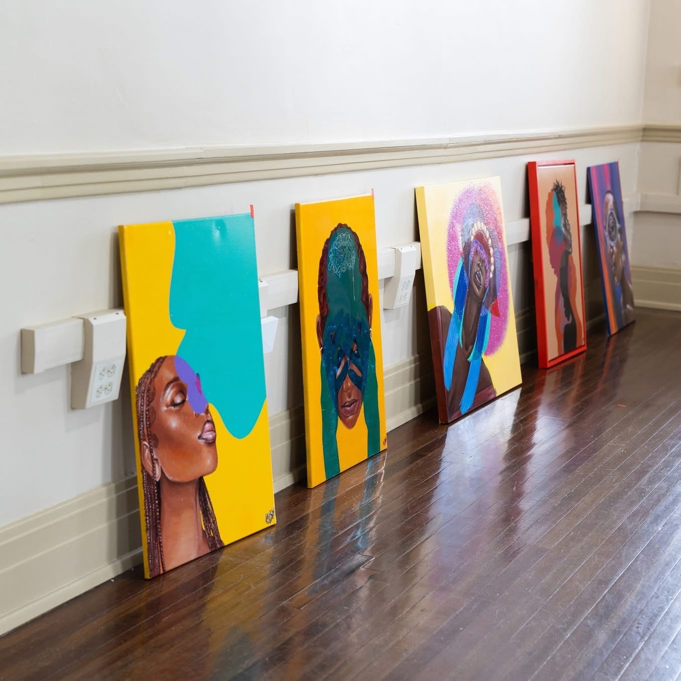 A series of colorful portrait artworks arranged along a wall inside Black Heritage Gallery